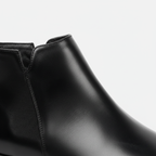 Close-up detail of men's black leather Chelsea boots showing elastic gusset and premium construction quality