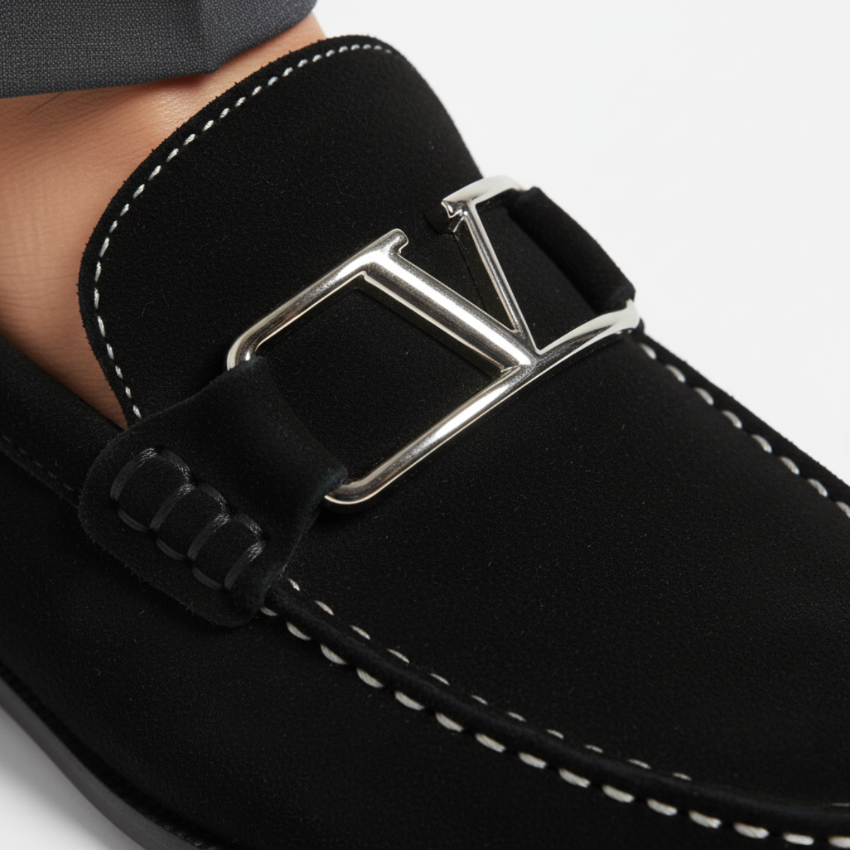 Close-up of black suede loafers showing silver metal buckle detail and hand-stitched moc-toe craftsmanship