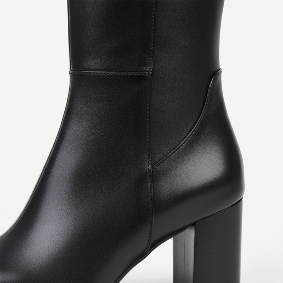 Close-up detail of black leather knee boot showing smooth finish and block heel