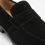 Close-up detail of black suede penny loafer showing keeper strap with diamond cutout and hand-stitching