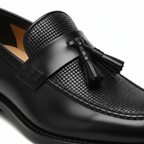 Close-up detail of black leather tassel loafer showing basket weave texture and decorative tassel accent