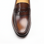 Close-up of cognac penny loafers showing hand-burnished leather finish and classic penny strap detail