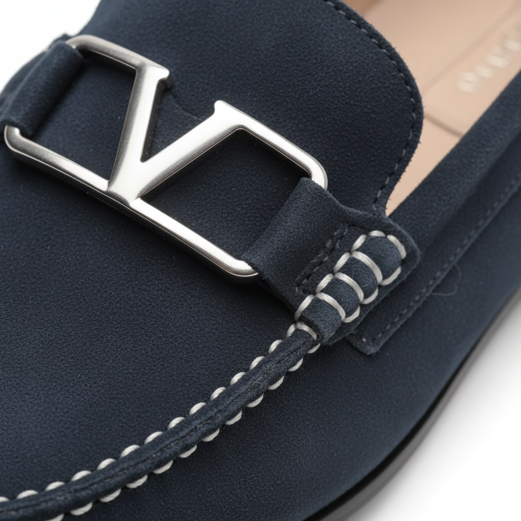 Close-up of navy suede loafers showing silver metal buckle detail and hand-stitched moc-toe craftsmanship